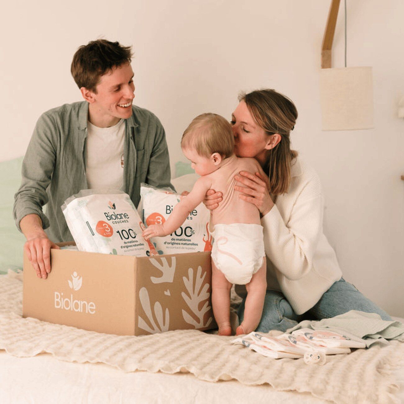 Parents et bébé ouvrant un colis d’abonnement couches Biolane dans le salon