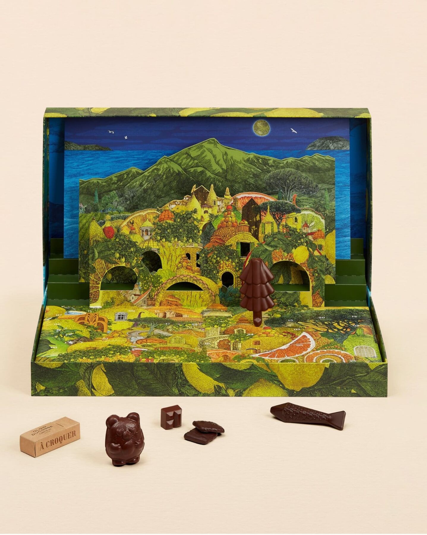 Le calendrier de l’Avent Alain Ducasse ouvert sur un village provençal en relief, avec un ourson, un poisson et des chocolats devant