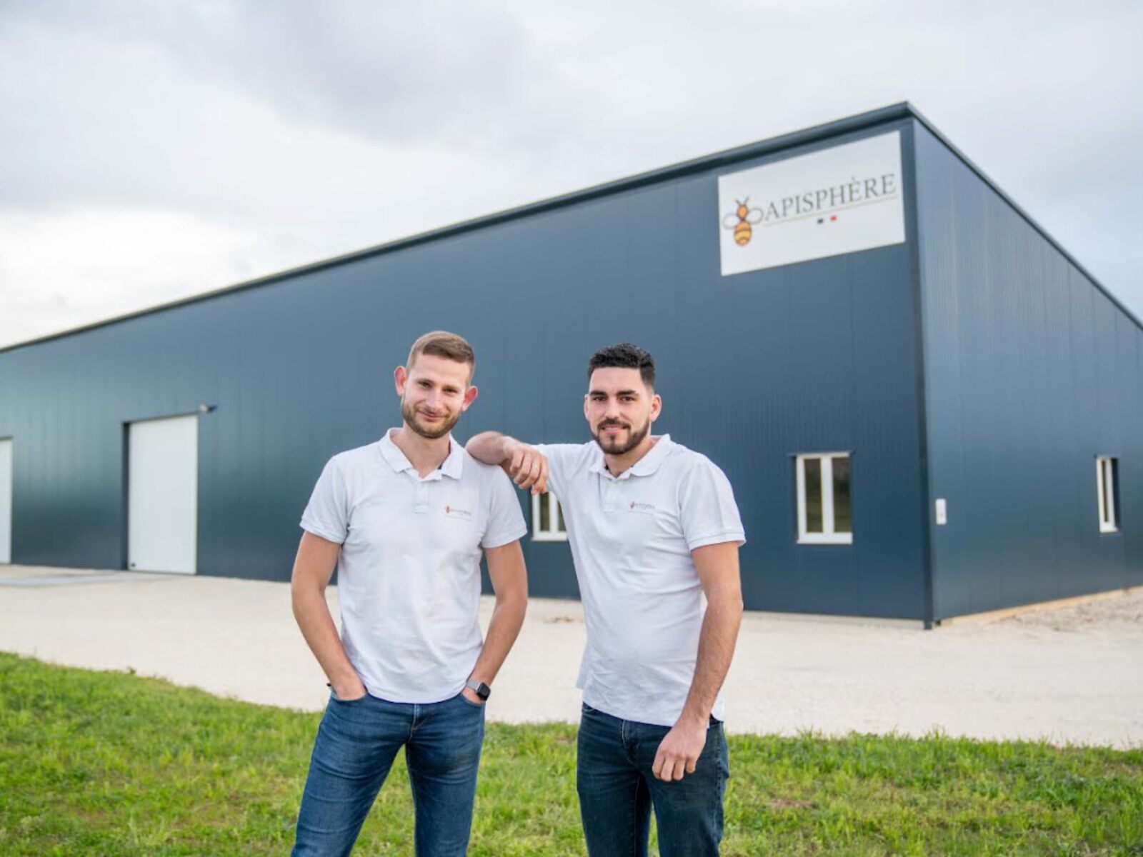 Deux jeunes hommes devant un bâtiment portant l’enseigne Apisphère
