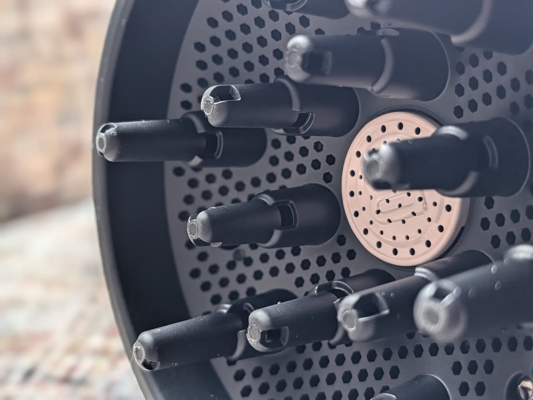 Gros plan sur les doigts du diffuseur Bellissima Diffon Ceramic et le disque en céramique rose au centre de la grille