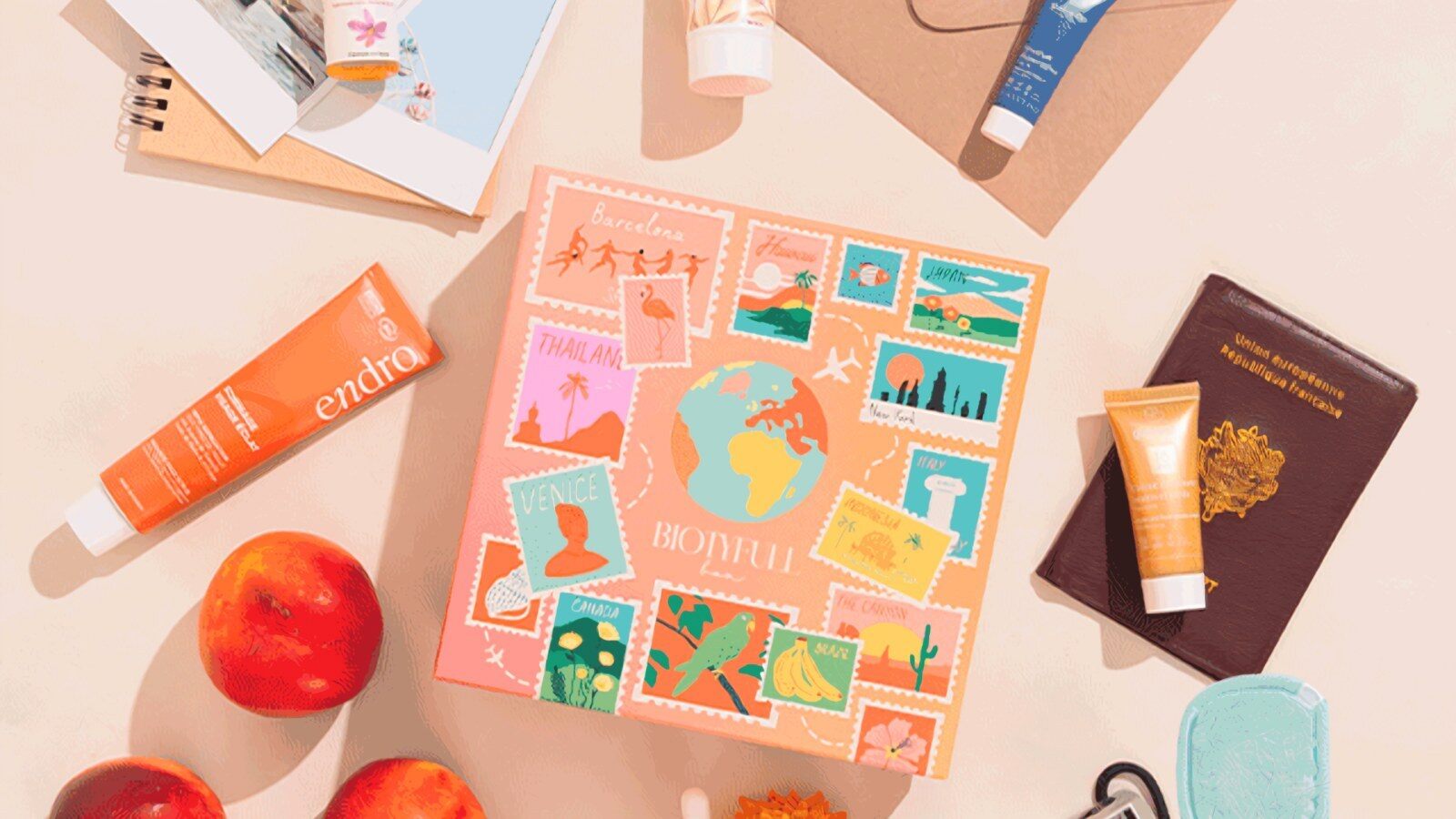 La Biotyfull Box Voyage autour du Monde posée sur une table entre des soins Endro, un passeport, des pêches et un carnet de voyage