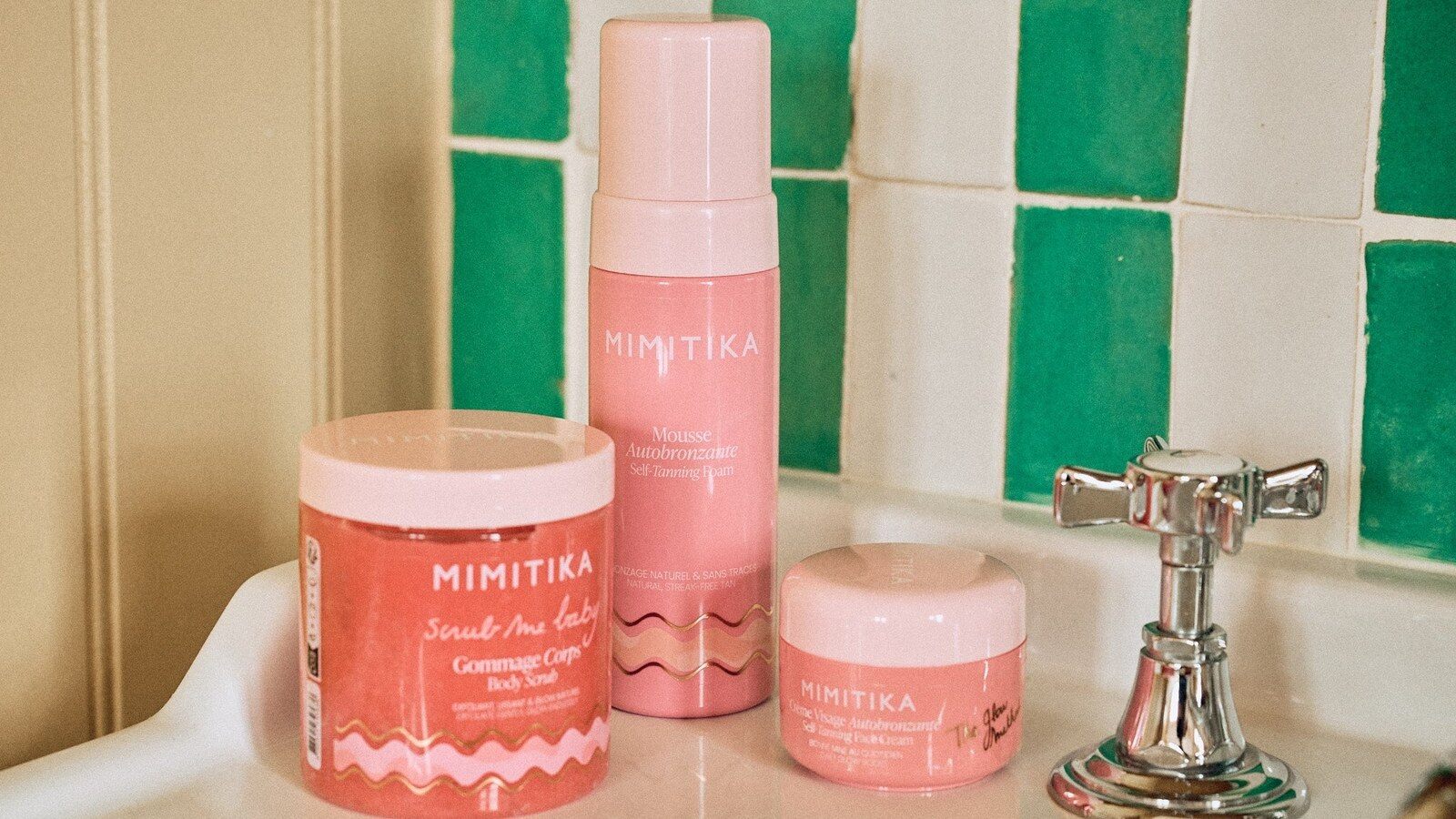Soins autobronzants Mimitika roses posés sur un lavabo devant un carrelage vert et blanc