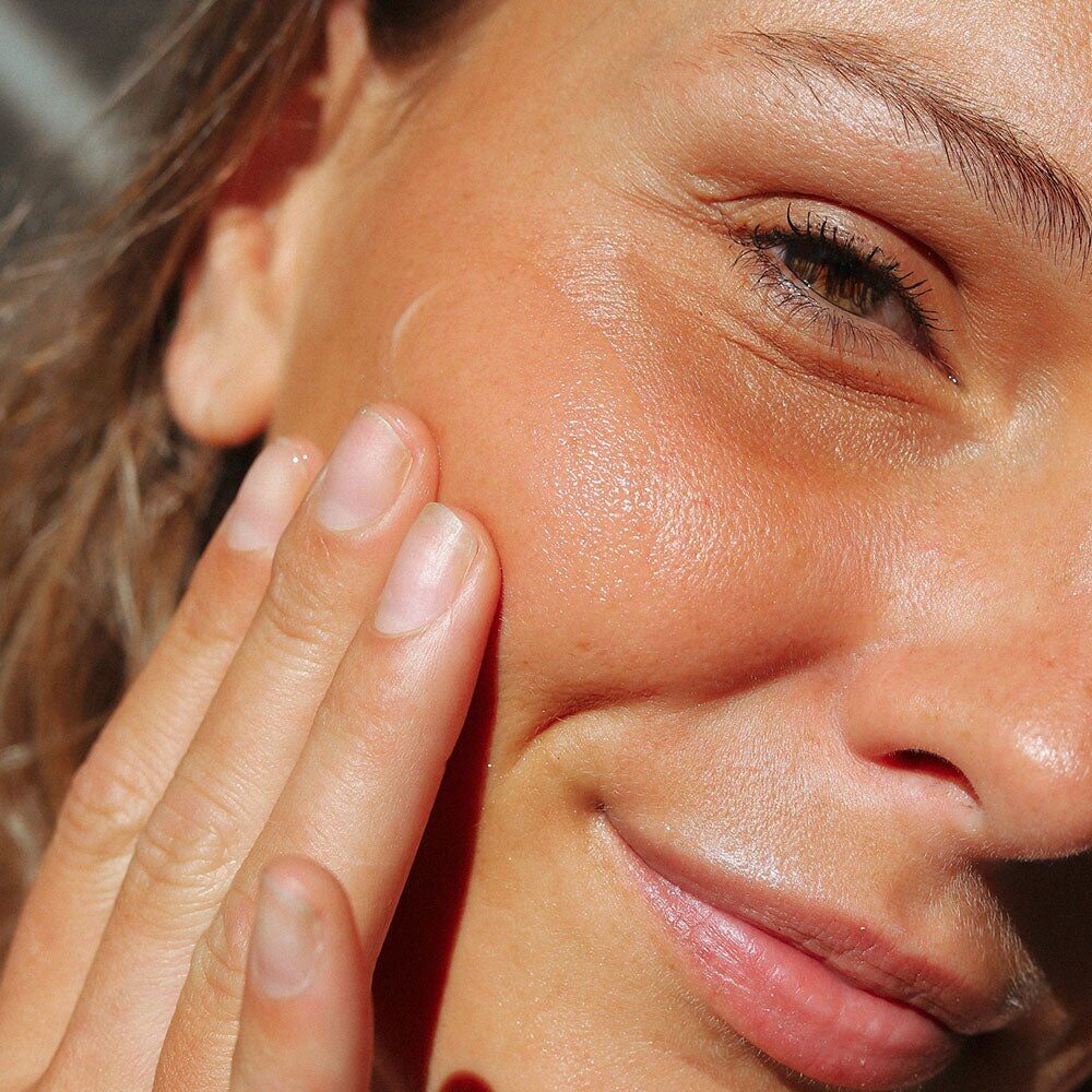 Une femme applique une crème sur sa joue, visuel de la crème visage autobronzante Mimitika