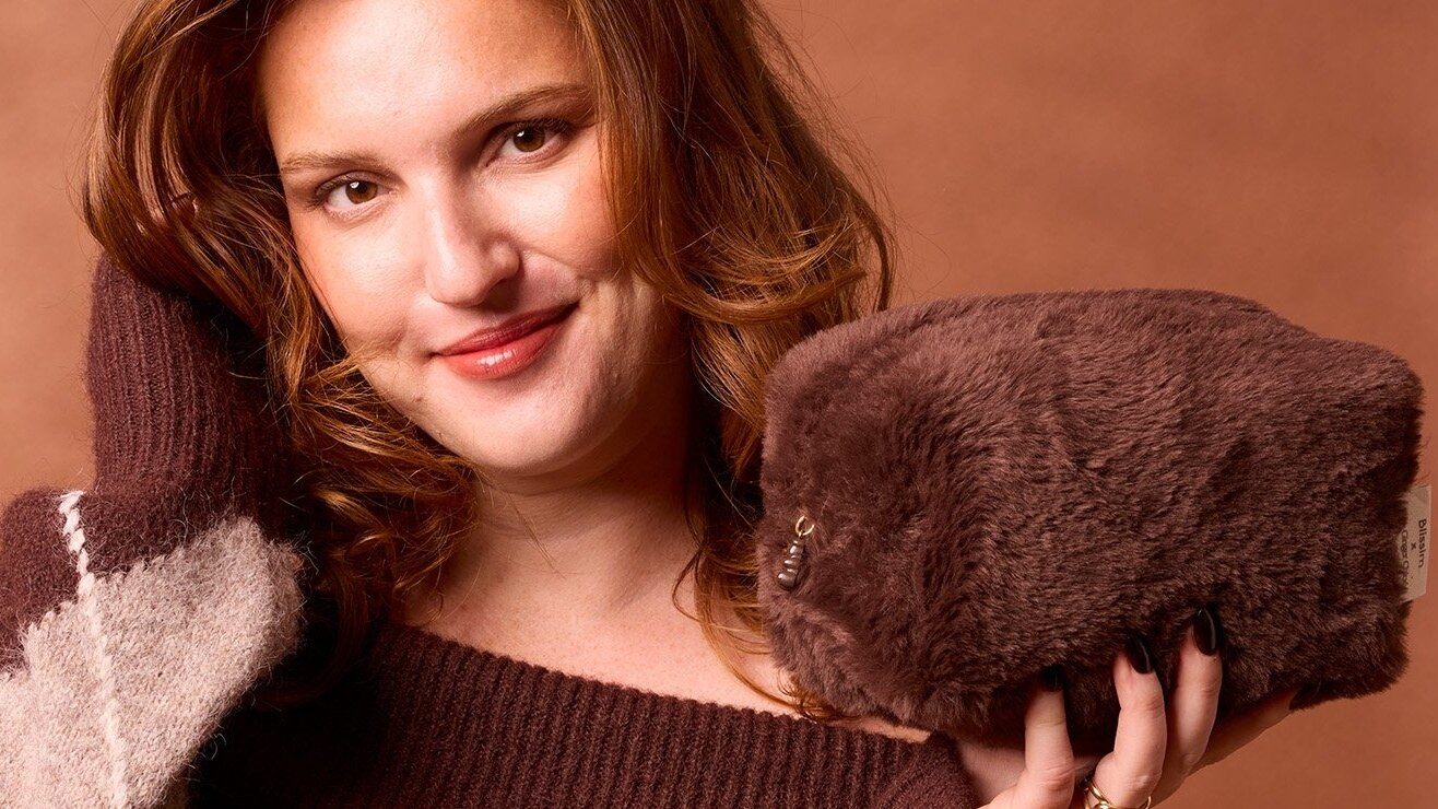 Chloé, de TheGingerChloé, souriante en pull bordeaux, tient la trousse chocolat façon fausse fourrure de l’édition Blissim