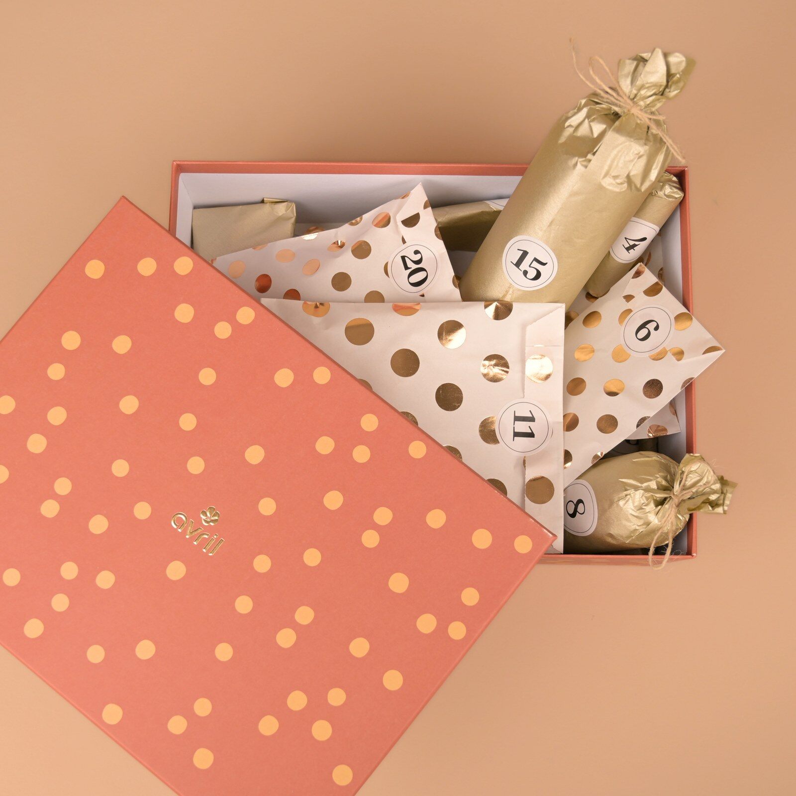 Coffret rose à pois dorés du calendrier de l’Avent Avril 2026 ouvert, avec ses pochettes numérotées en papier doré et kraft