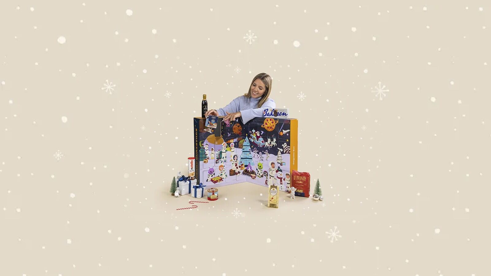 Une femme ouvre le calendrier de l’Avent Degusta Box 2026 au décor spatial, entouré de produits d’épicerie
