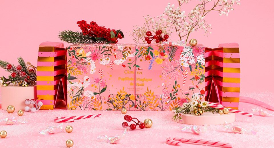 Le calendrier de l’Avent Glowria 2026, une papillote géante rose aux extrémités rayées rose et or, posée dans un décor de Noël avec des sucres d’orge et des baies rouges