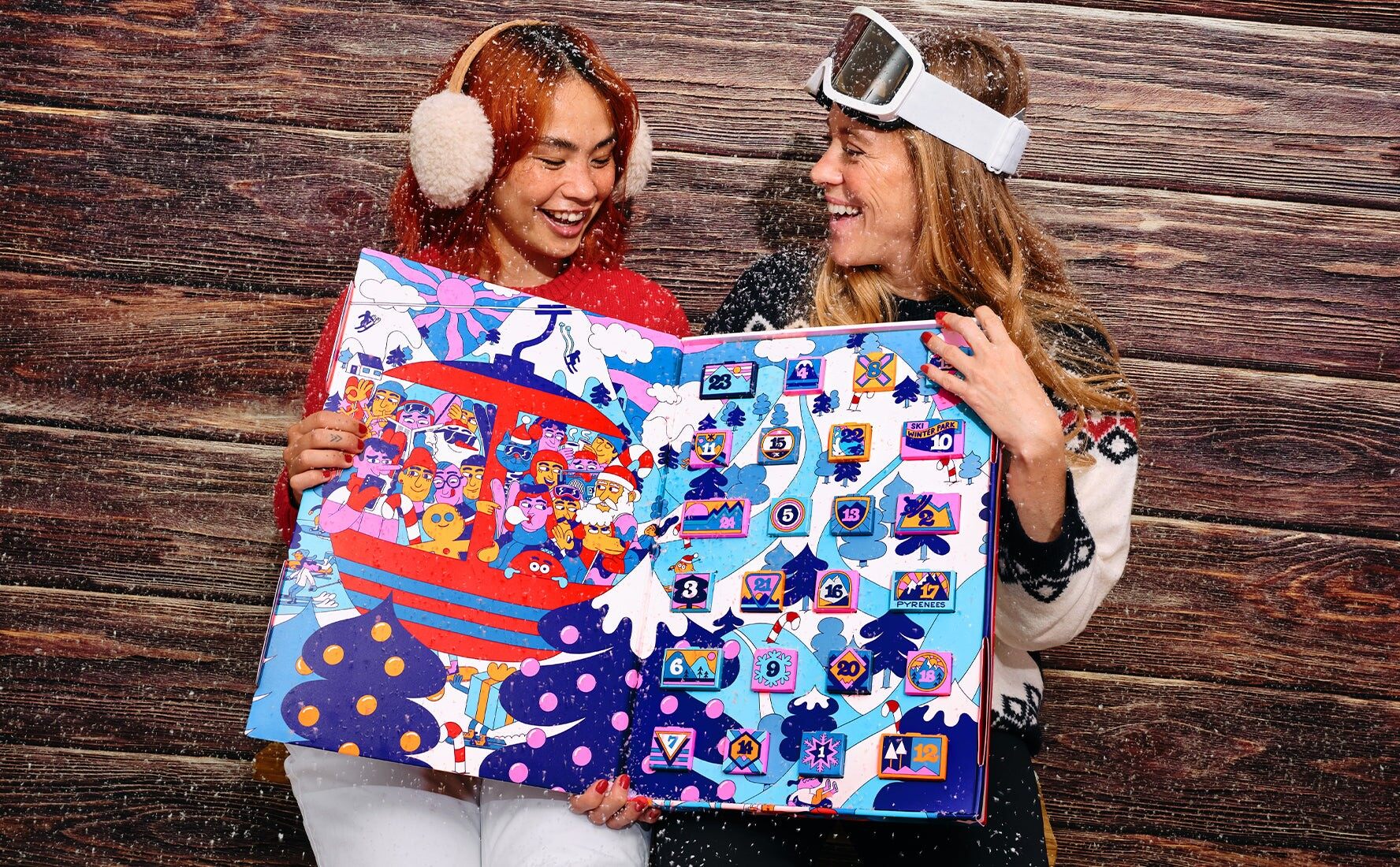 Deux femmes en tenue de ski tiennent le calendrier de l’Avent Noël à ski du Chocolat des Français ouvert