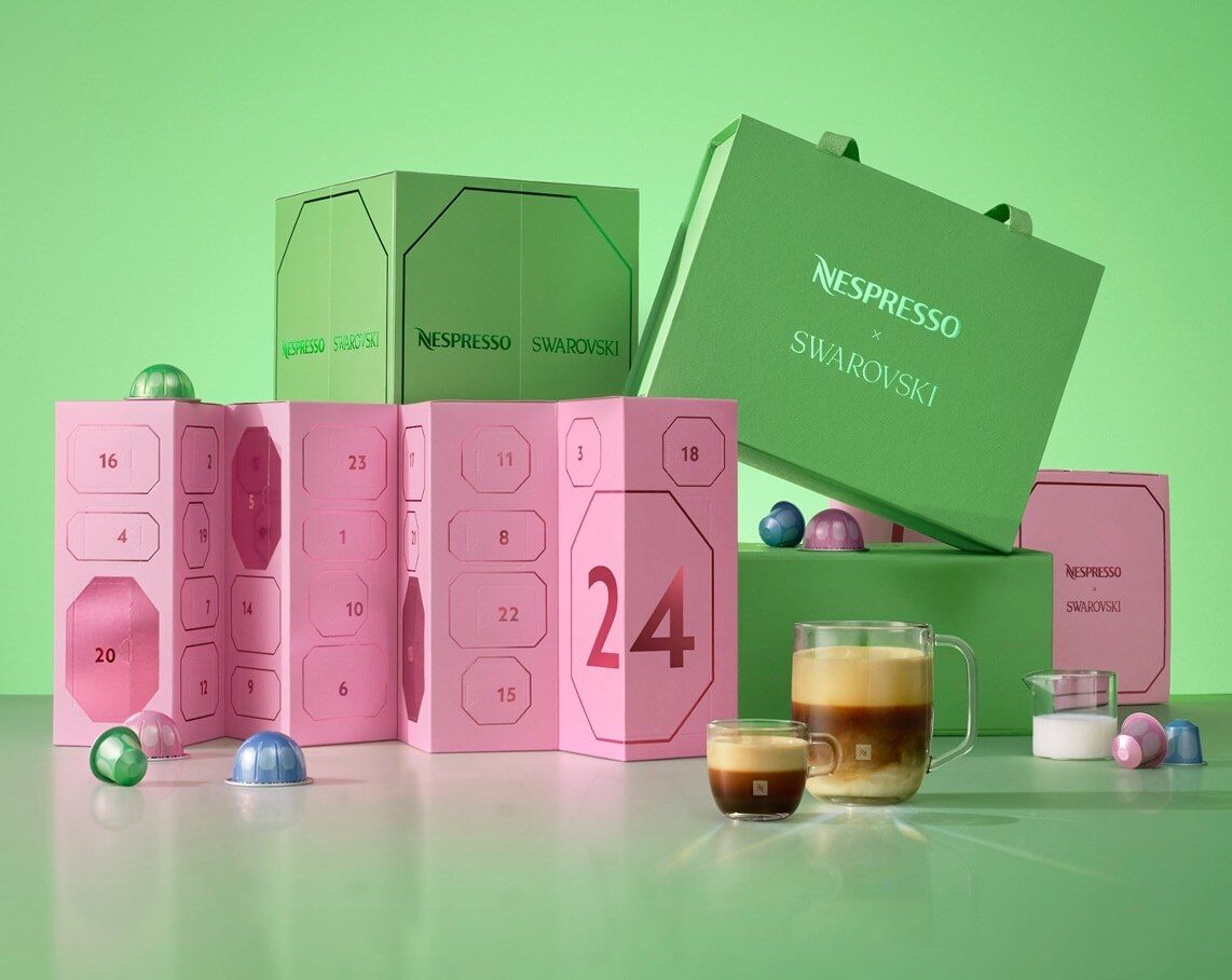 Calendriers de l’Avent Nespresso x Swarovski 2026 rose et vert sur fond vert, avec une tasse de café