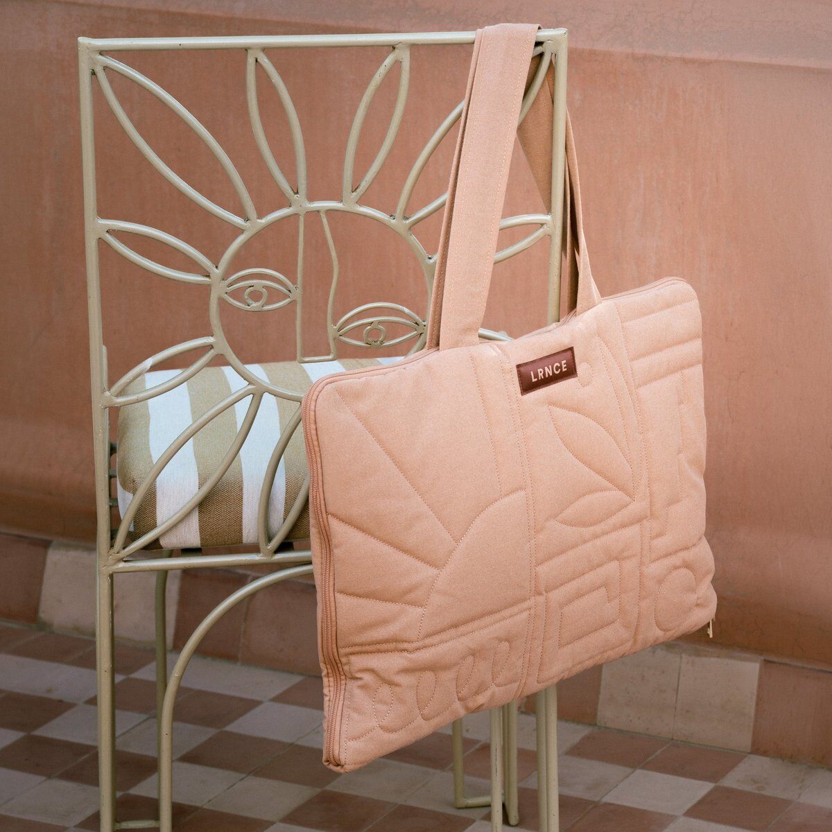 Le calendrier de l’Avent Oh My Cream x LRNCE refermé en sac matelassé terracotta, suspendu à une chaise en métal
