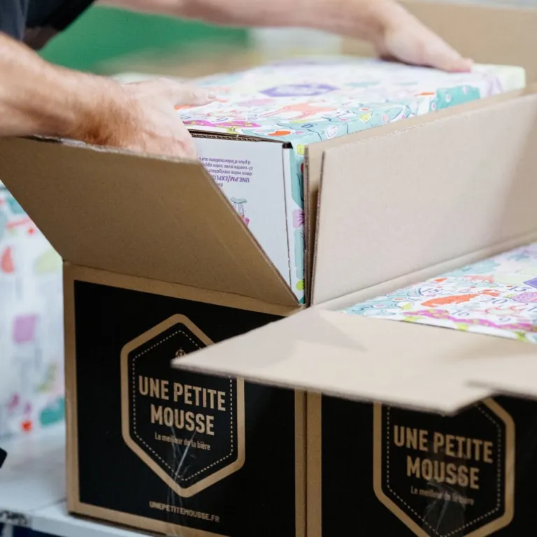 Une personne ouvre le carton d’expédition noir Une Petite Mousse contenant le calendrier de l’Avent bières 2026