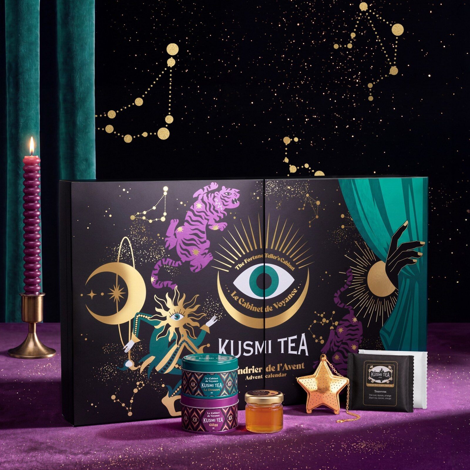 Le calendrier de l’Avent Kusmi Tea 2026 Cabinet de Voyance, coffret violet et doré orné d’un œil, devant un rideau de théâtre, avec un infuseur étoile et un pot de thé à tartiner