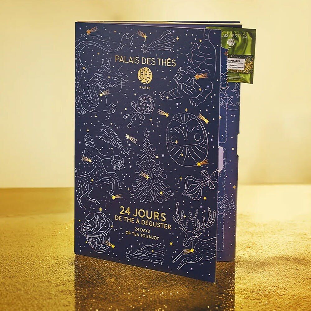 Le calendrier de l’Avent Palais des Thés 2026, en forme de livre bleu nuit à constellations dorées, ouvert sur ses cases numérotées et quelques mousselines de thé