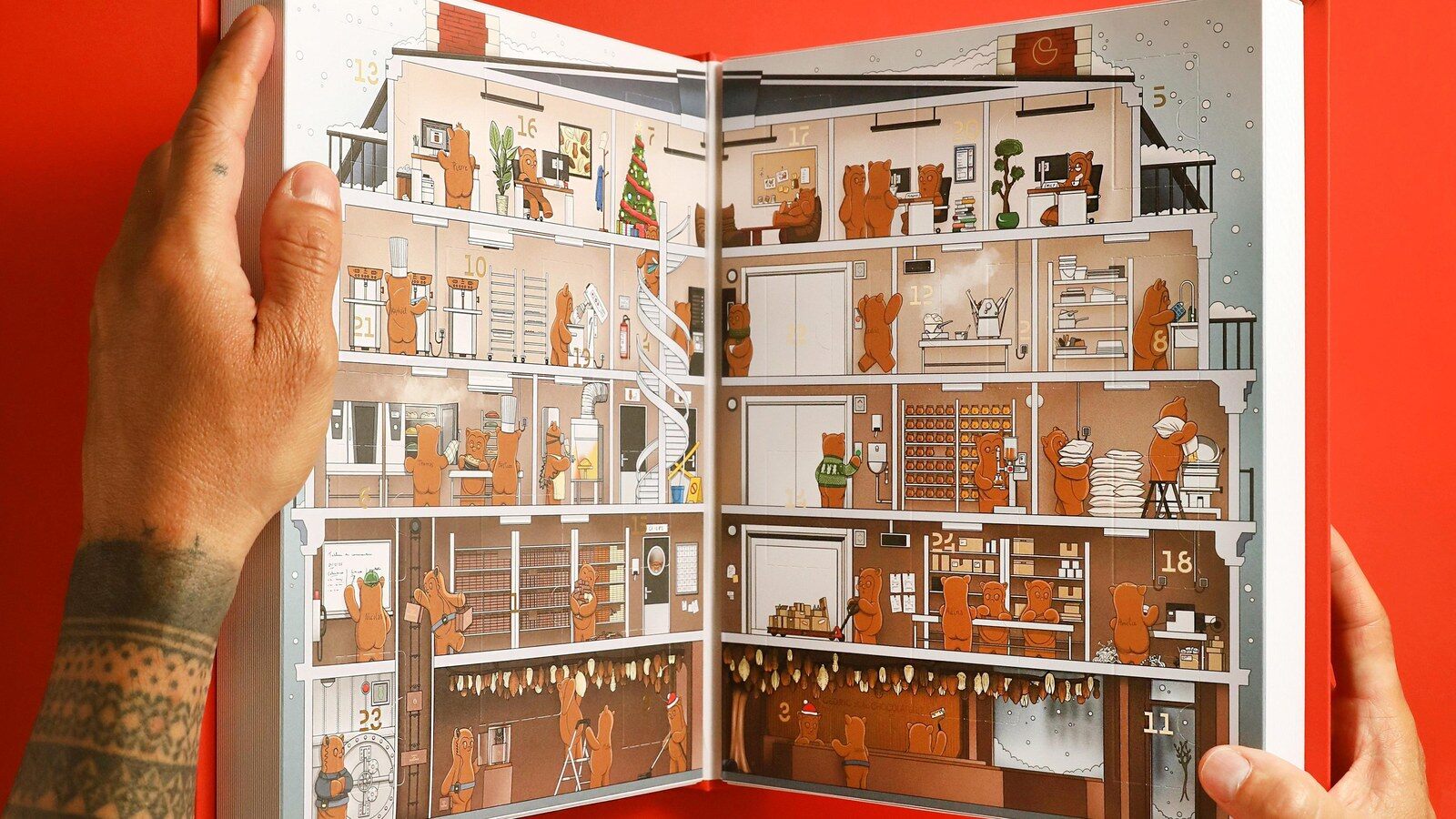 Deux mains tiennent ouvert le calendrier de l’Avent Tome 2 de Cédric et la Chocolaterie, une chocolaterie illustrée peuplée d’oursons, sur fond rouge