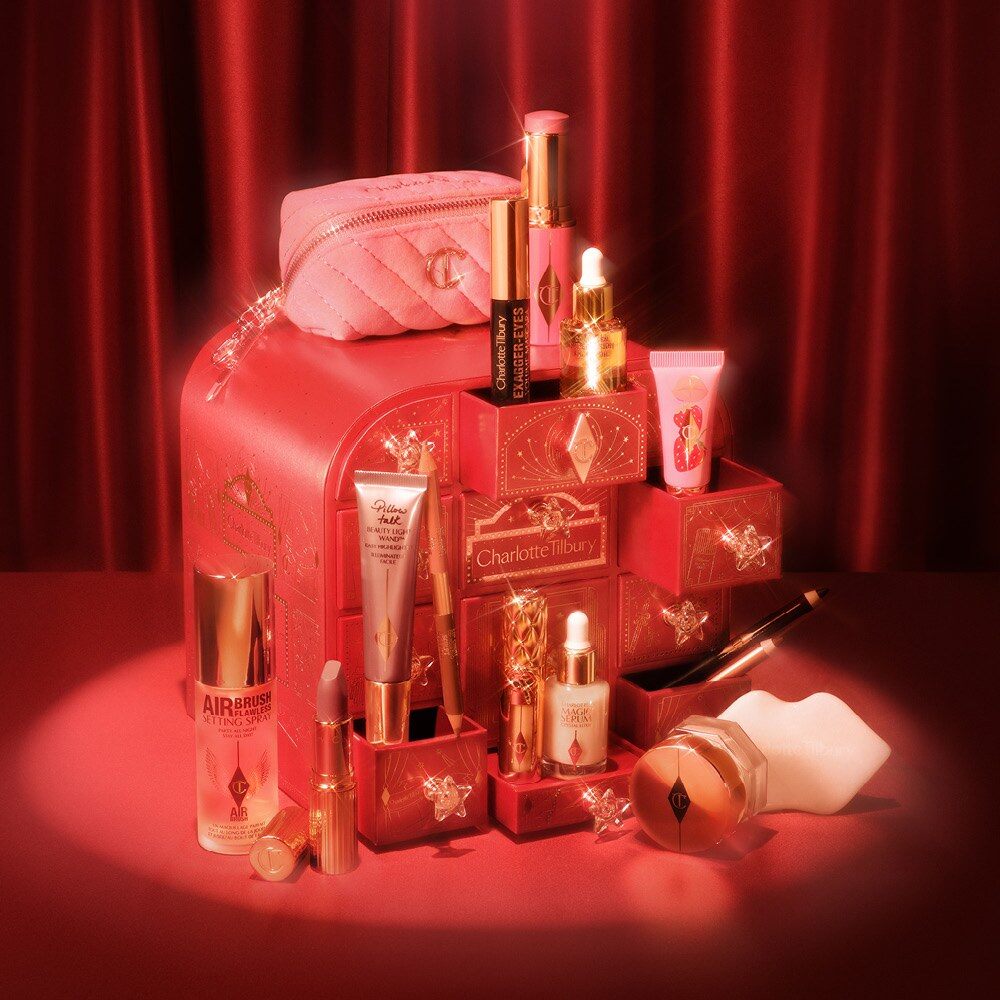 Le calendrier de l’Avent Charlotte Tilbury 2026 ouvert devant un rideau rouge, entouré de ses produits et de la trousse rose