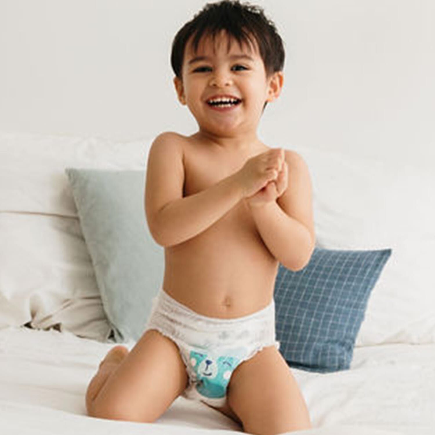 Petit garçon souriant portant une couche Biolane, assis sur un lit