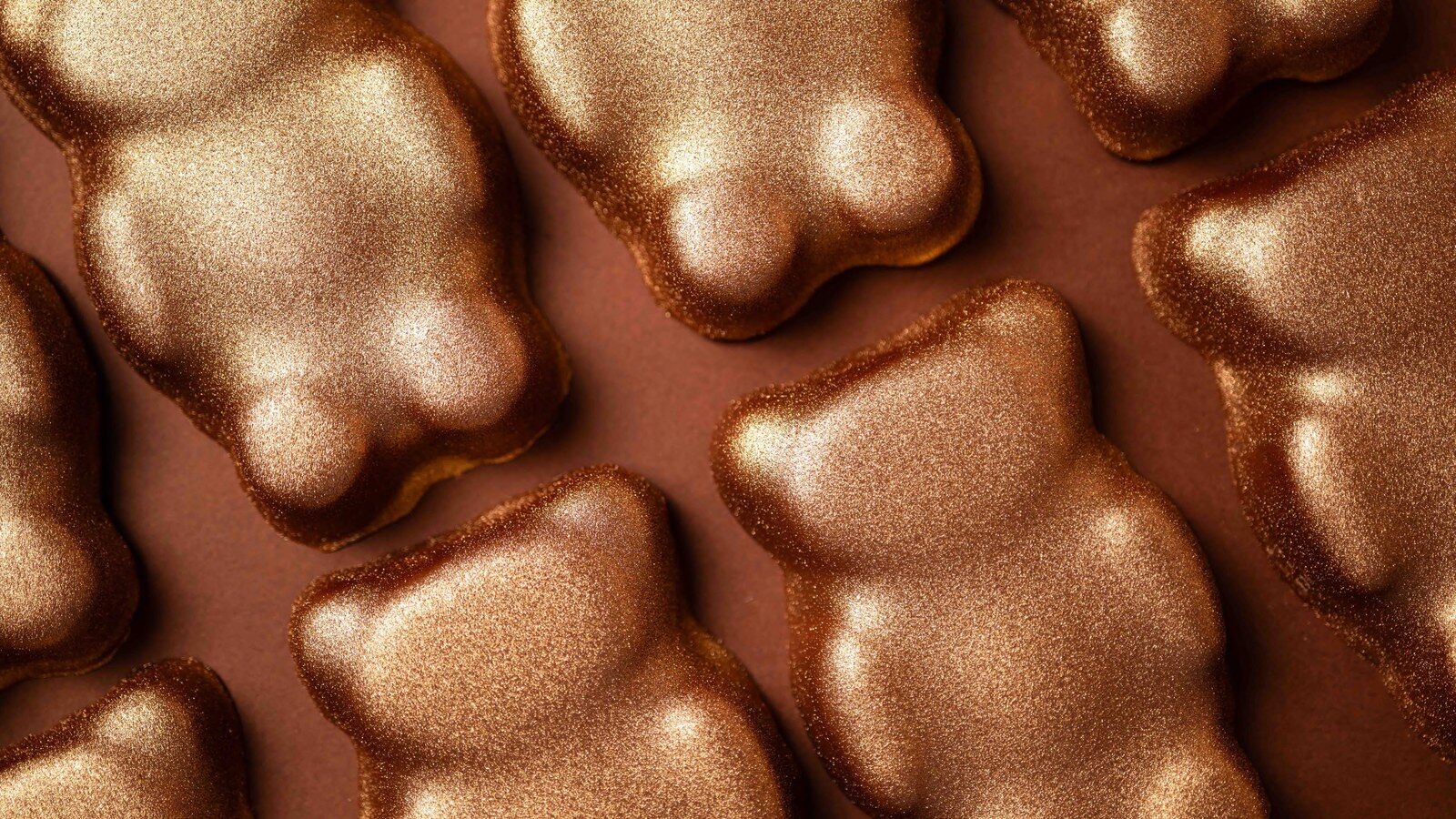 Oursons guimauve dorés de La Pâtisserie Cyril Lignac alignés sur un fond chocolat
