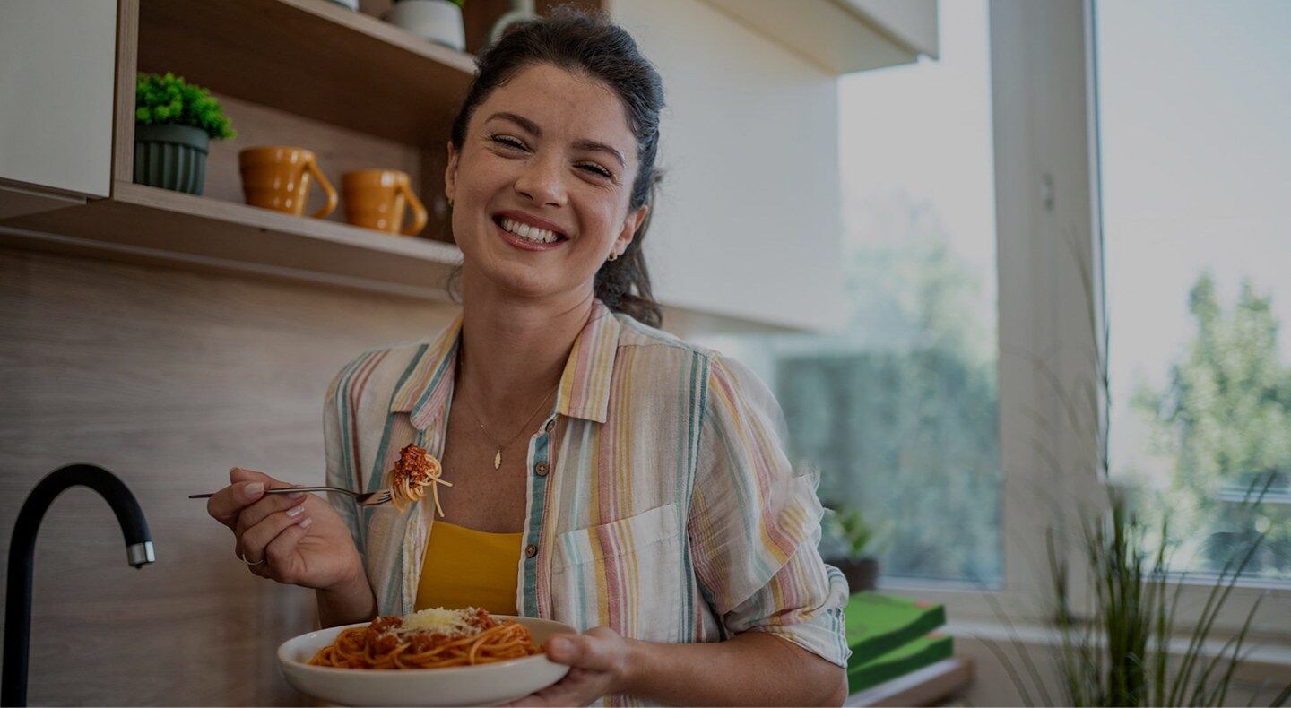 Une femme souriante mange un plat Dietbon dans sa cuisine