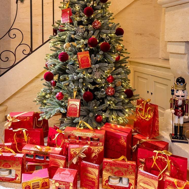 Un sapin de Noël décoré de boules rouges, entouré de coffrets cadeaux Durance rouges et dorés et d’un casse-noisette