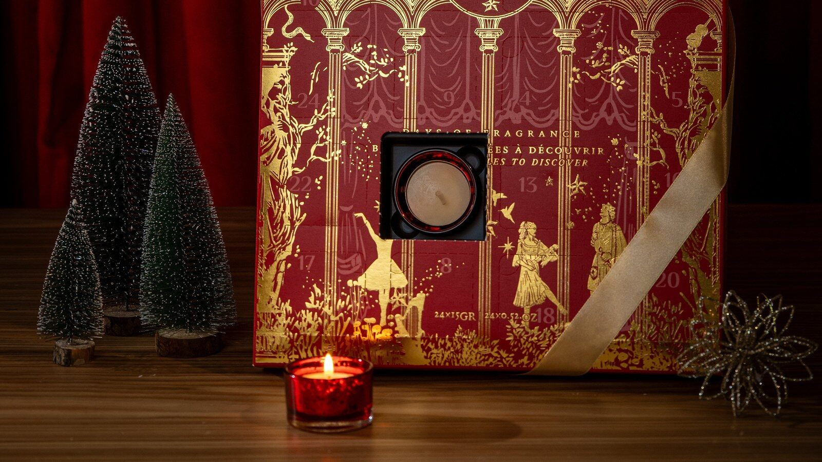 Le calendrier de l’Avent bougies Durance 2026 rouge et or, une case ouverte sur une bougie chauffe-plat, entre de petits sapins et un photophore allumé
