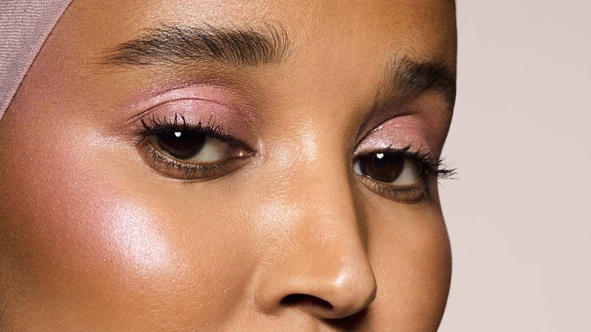 Gros plan d’un visage maquillé avec l’enlumineur Killawatt de Fenty Beauty, reflets roses sur les pommettes et fard rosé sur les paupières