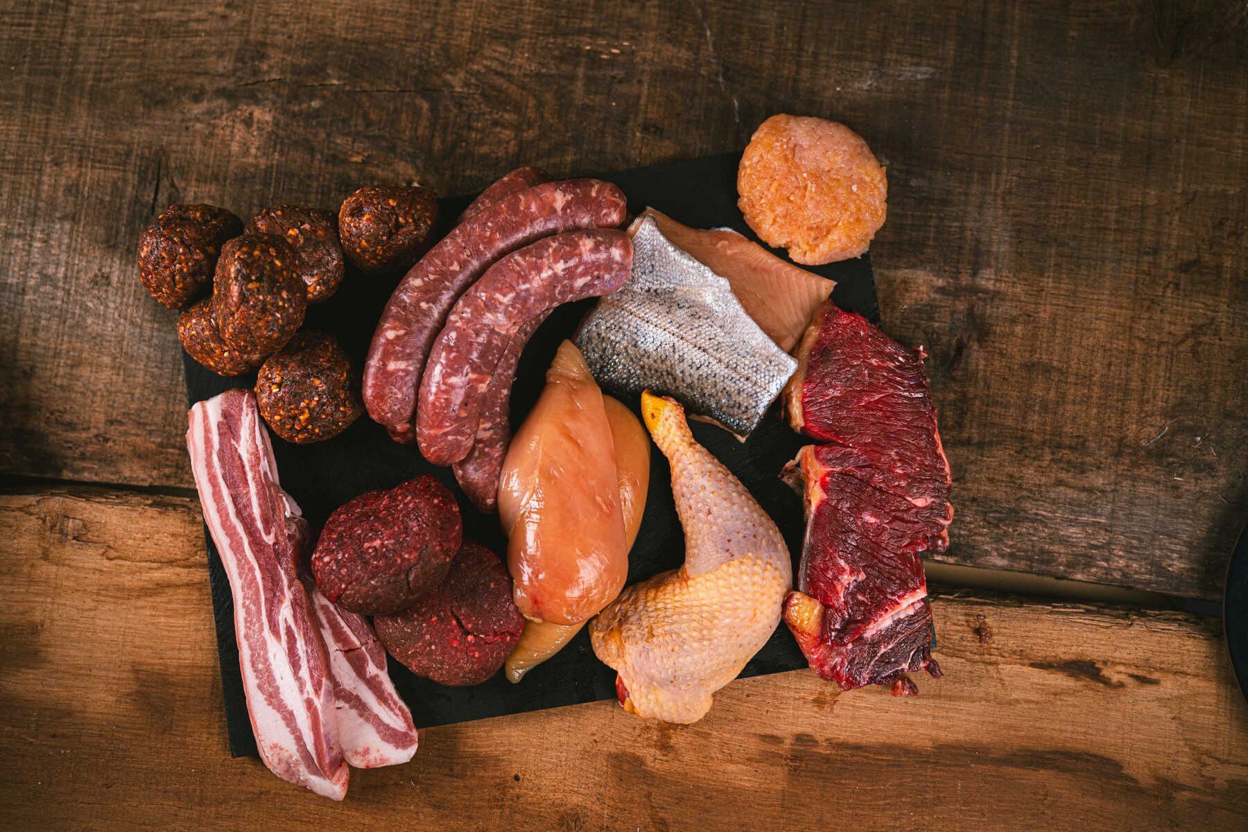 Le contenu d’une box Féroce posé sur une planche en bois : saucisses, filets de poulet, filet de truite, poitrine de porc, steaks et boulettes
