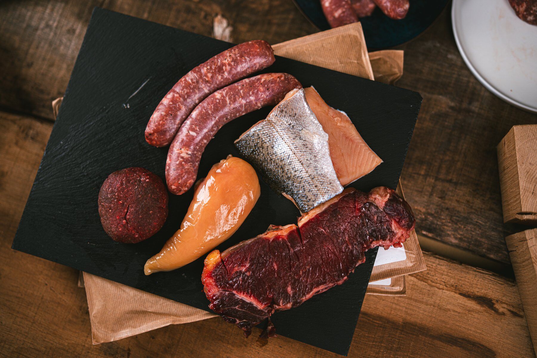Une box Féroce M : saucisses, filet de poulet, filet de truite, steak et morceau de bœuf sur une ardoise