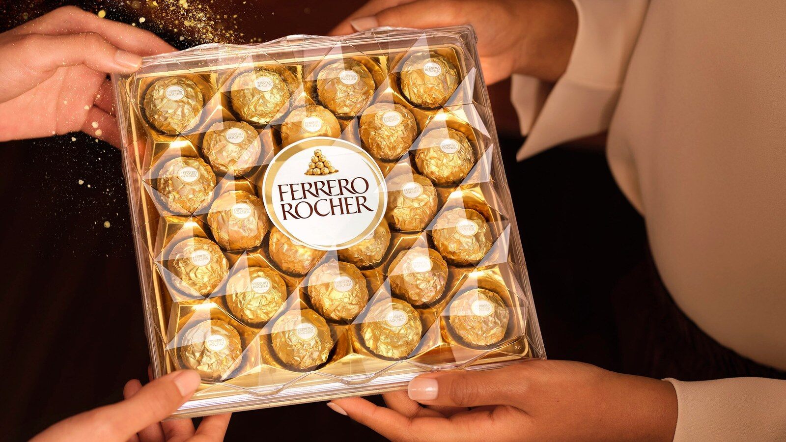 Deux personnes se passent une boîte de 24 Ferrero Rocher dorés dans une ambiance de fête aux bougies