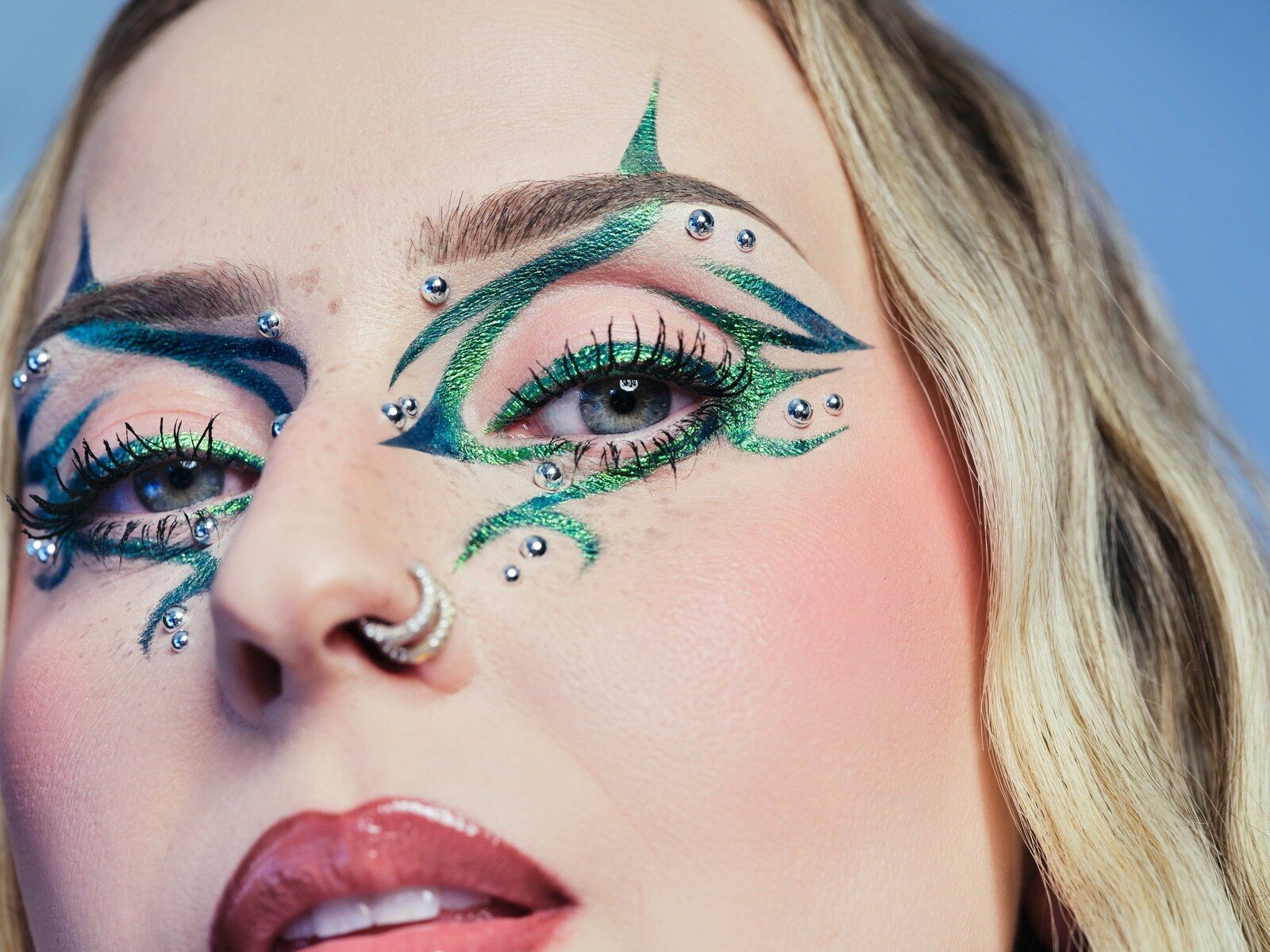 Une femme maquillée d’un eyeliner graphique vert et bleu orné de strass