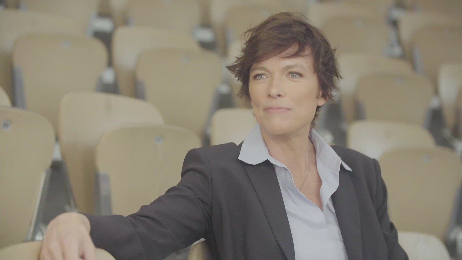 Anne Le Nen en veste de costume assise dans des tribunes vides de stade