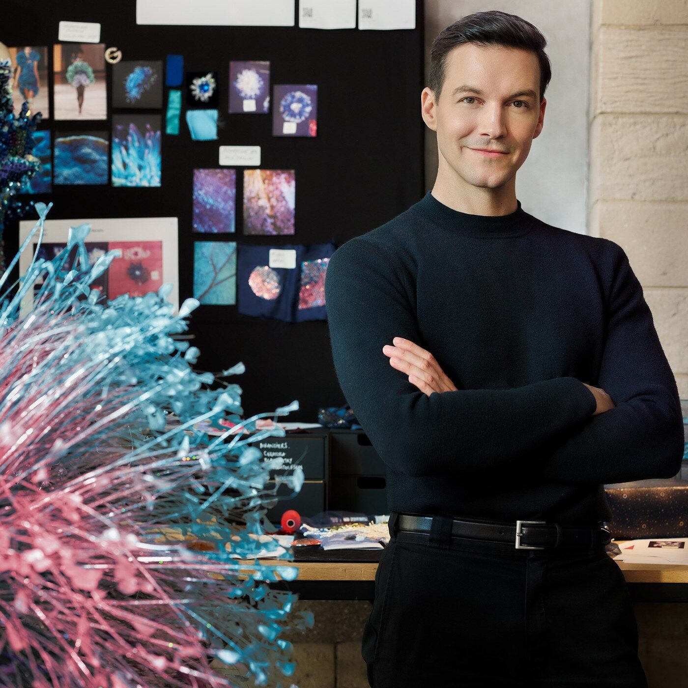 Le couturier Kévin Germanier posant bras croisés dans son atelier, devant un mur d’inspirations