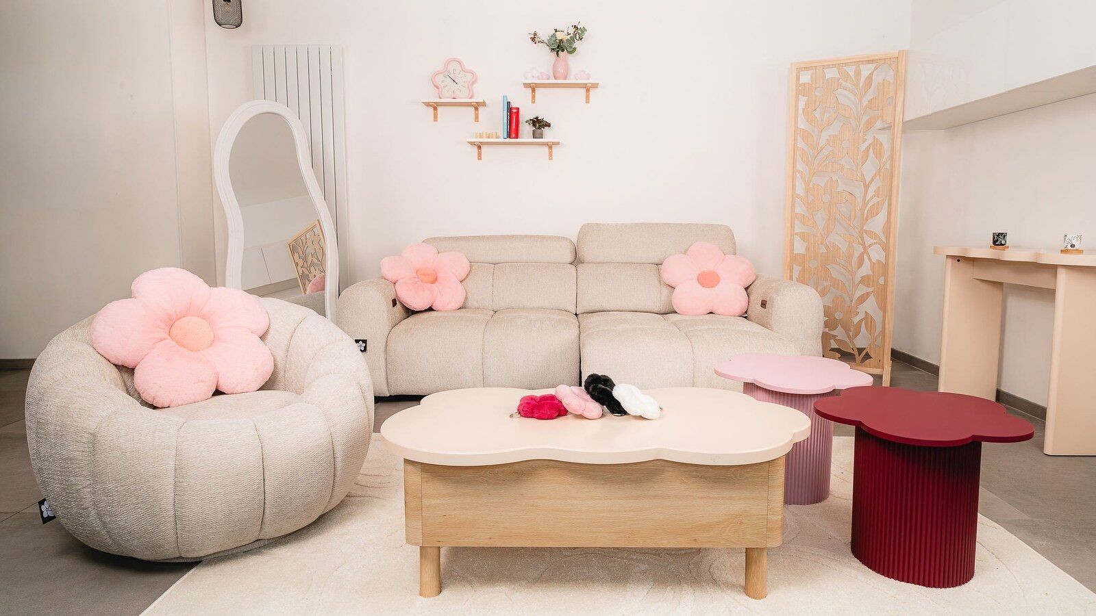 Salon de la collection Hayami x Conforama avec canapé beige, fauteuil rond, coussins fleurs roses, table basse en forme de fleur et paravent