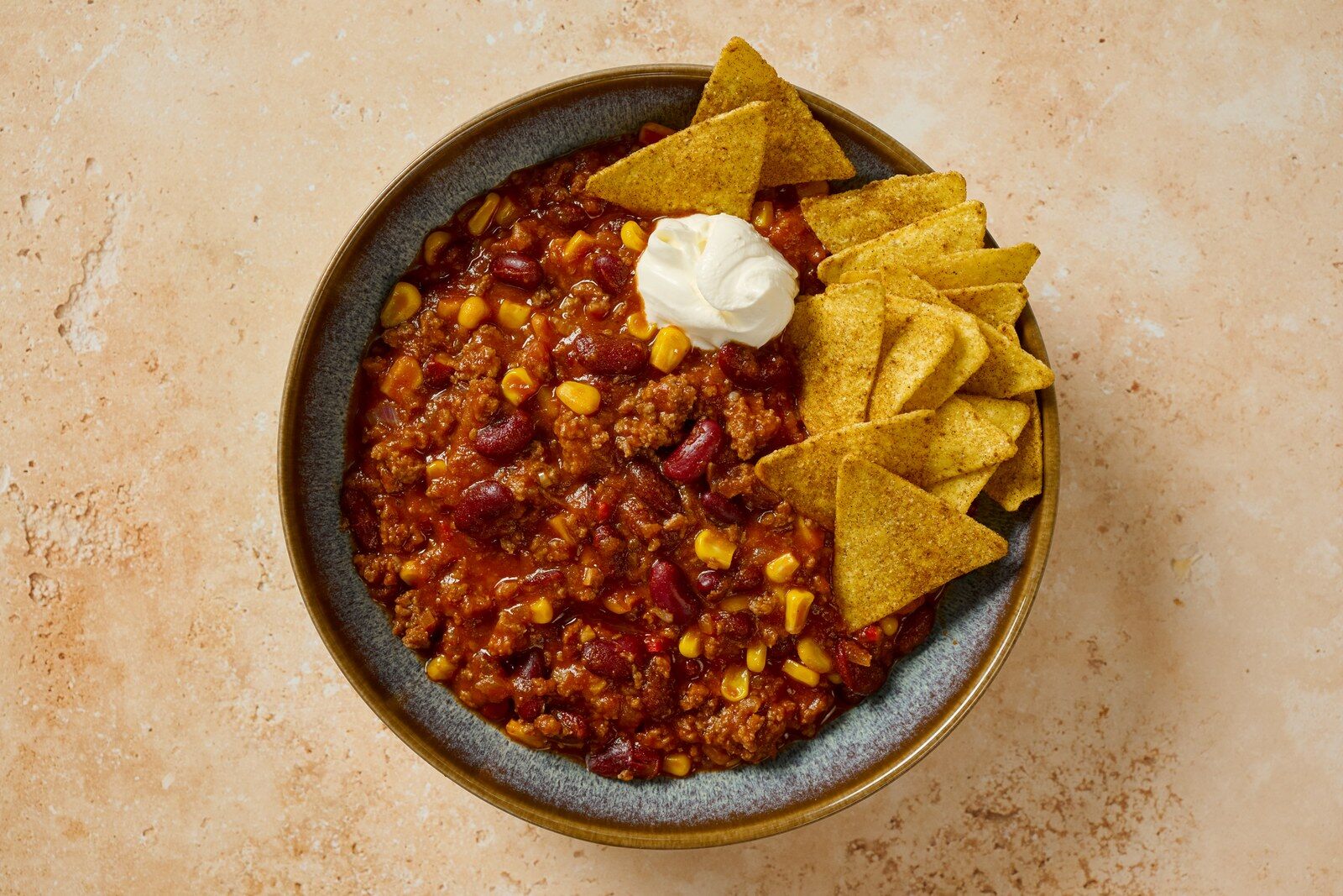 Bol de chili con carne garni de crème et de chips de tortillas, sur une table en pierre