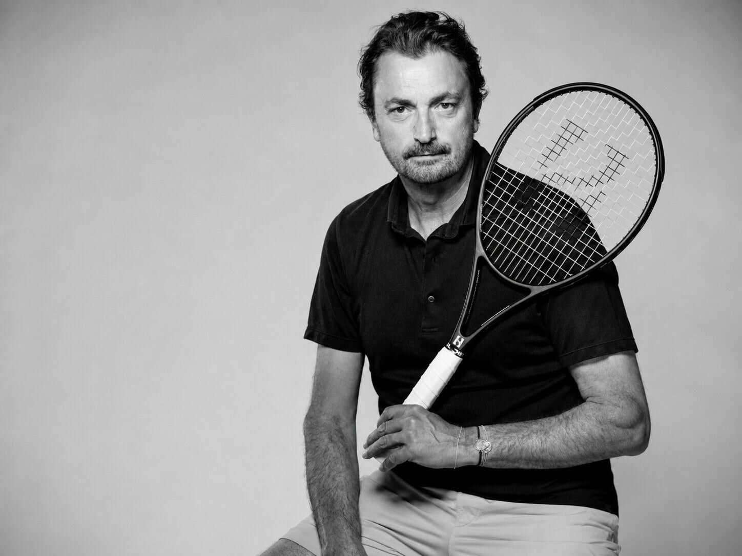 Portrait en noir et blanc d’Henri Leconte en polo, une raquette posée sur l’épaule