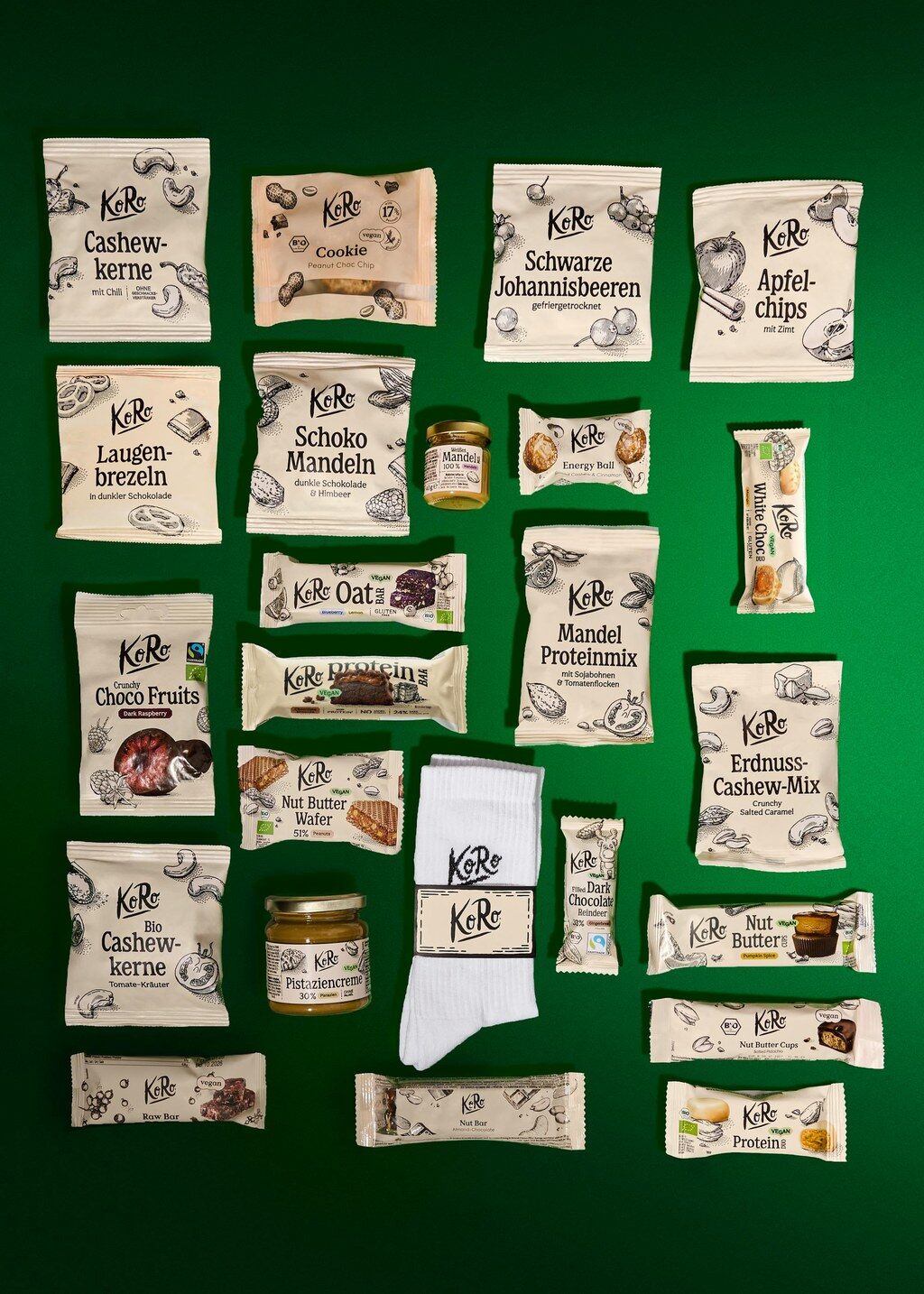 Les produits du calendrier de l’Avent vegan KoRo 2026 étalés sur fond vert, dont une paire de chaussettes