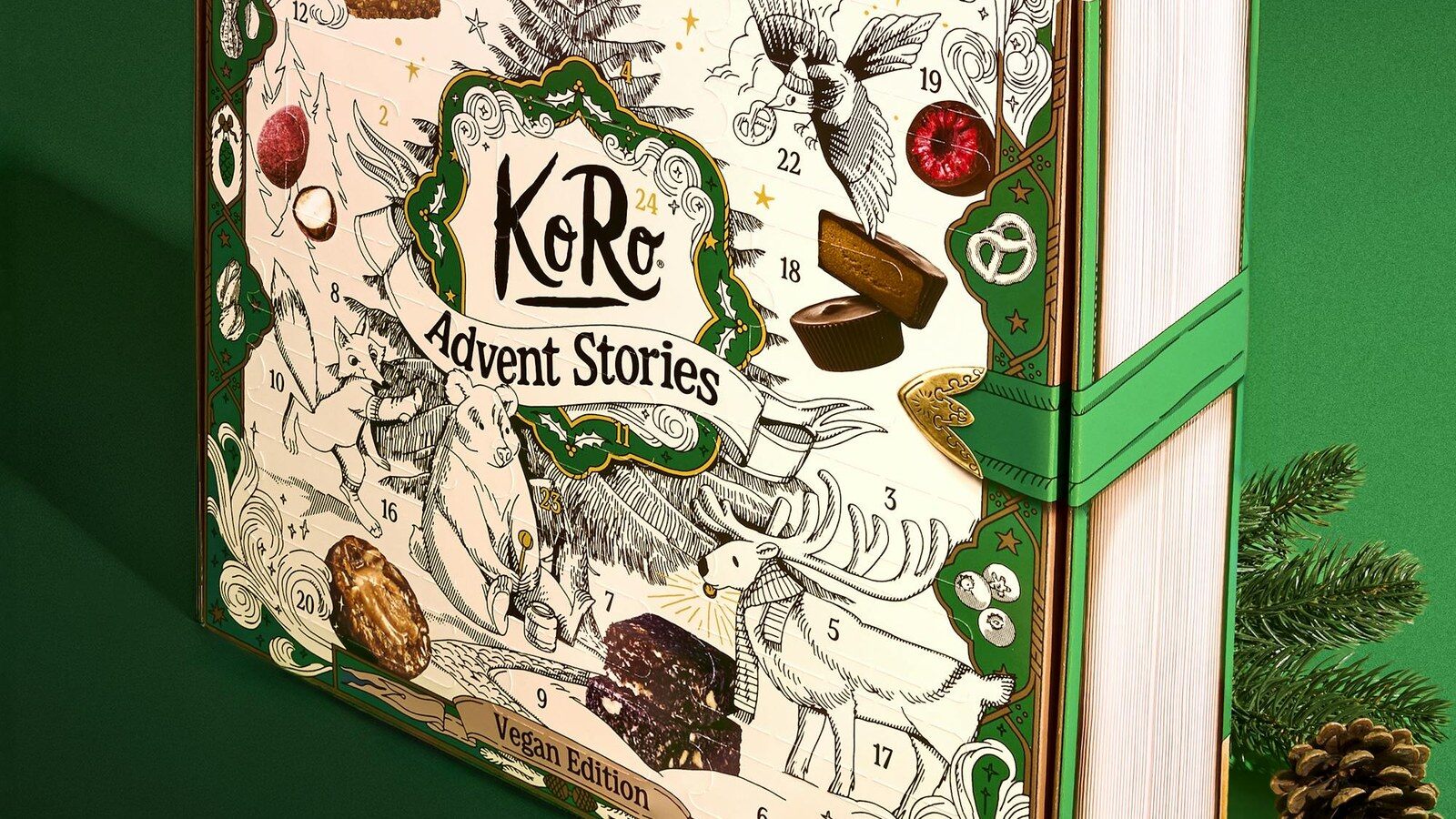 Le calendrier de l’Avent vegan KoRo 2026 Advent Stories posé sur fond vert près d’une pomme de pin