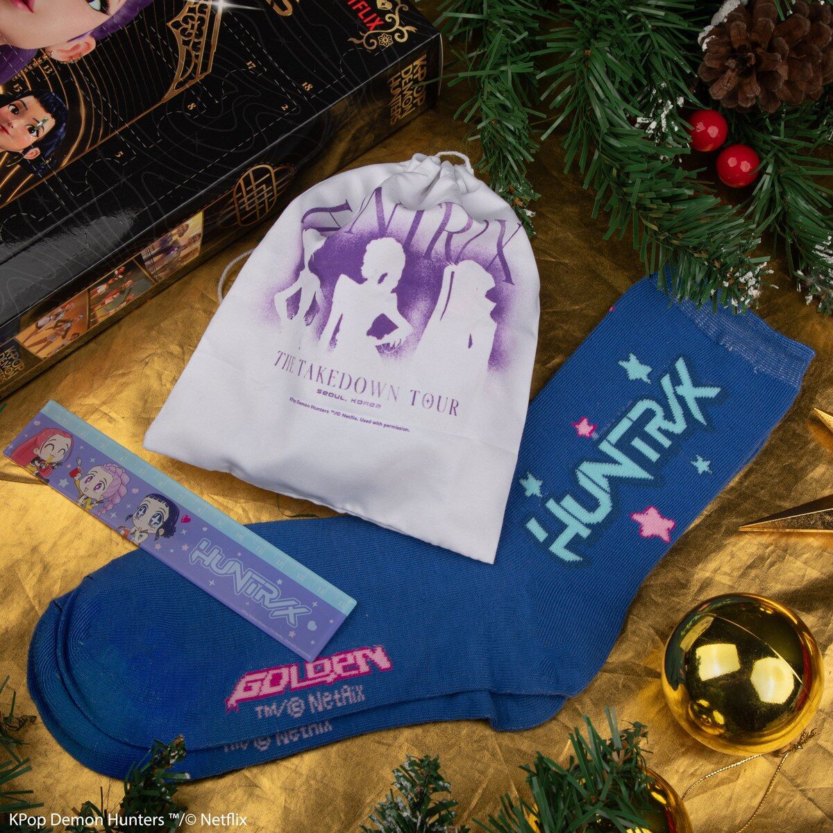 Des chaussettes bleues HUNTR/X, un pochon blanc The Takedown Tour et une règle posés à côté du calendrier de l’Avent KPop Demon Hunters 2026