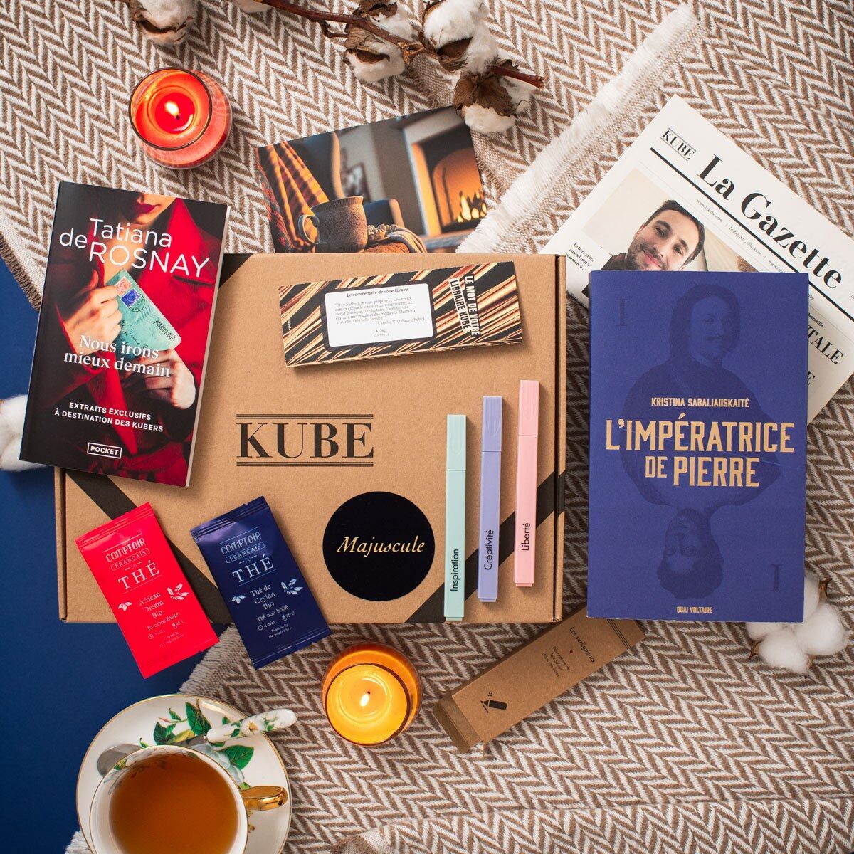 Une Kube Majuscule ouverte avec un roman grand format, La Gazette, des sachets de thé, des surligneurs et une tasse de thé