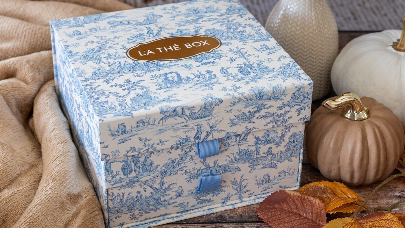 Coffret Maison de Famille de La Thé Box en toile de Jouy bleue posé près de citrouilles et d’un plaid