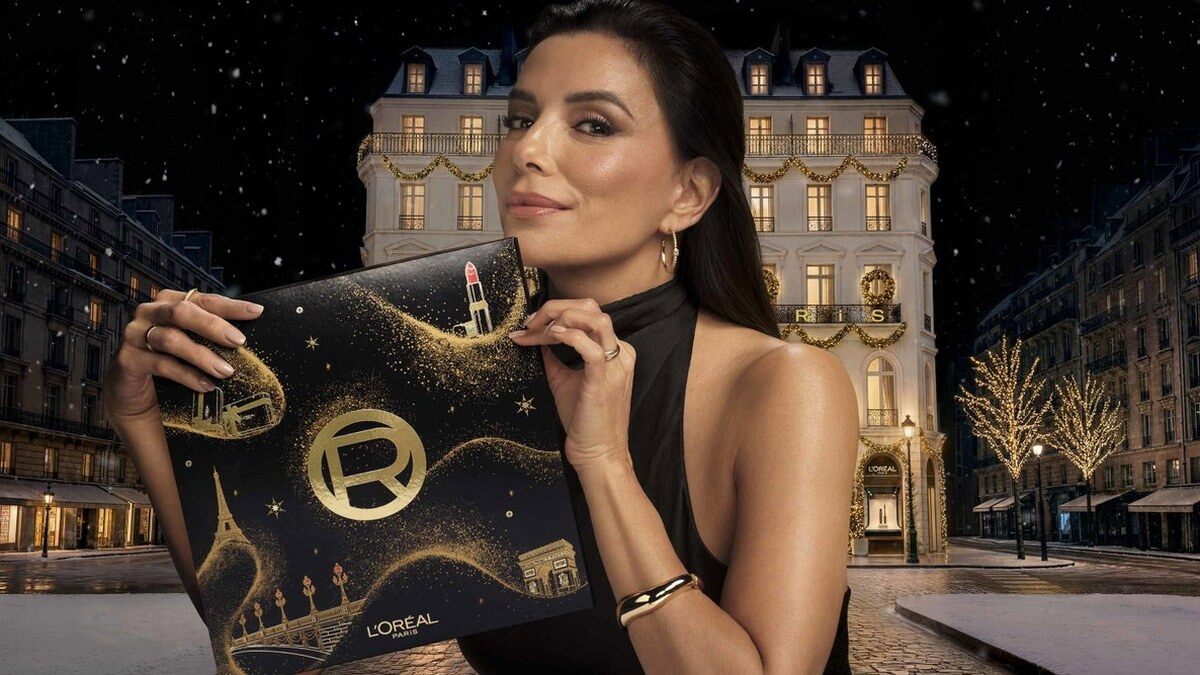Une femme en robe noire tient le calendrier de l’Avent L’Oréal Paris 2026 dans une rue de Paris enneigée et illuminée