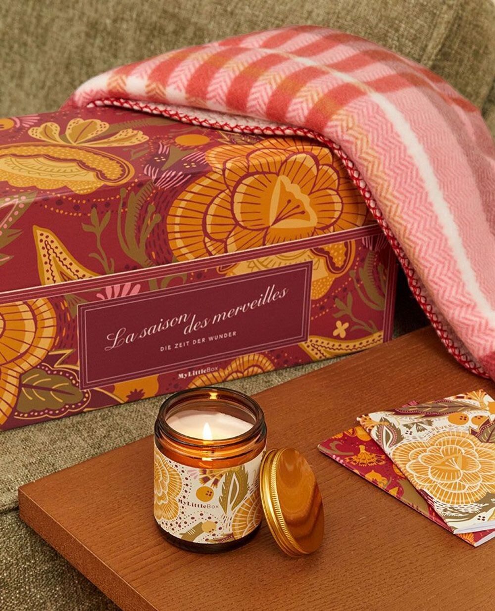 La Double Box My Little Box « La Saison des merveilles » posée sur un canapé, à côté d’une bougie et d’un plaid rose