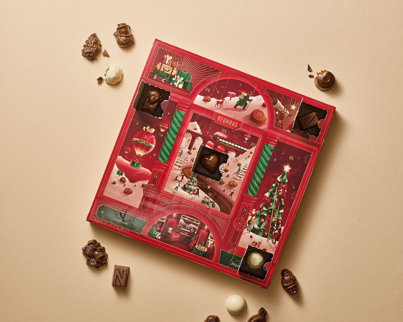 Le calendrier de l’Avent Classique Neuhaus 2026, rouge et illustré, entouré de pralines et de figurines en chocolat