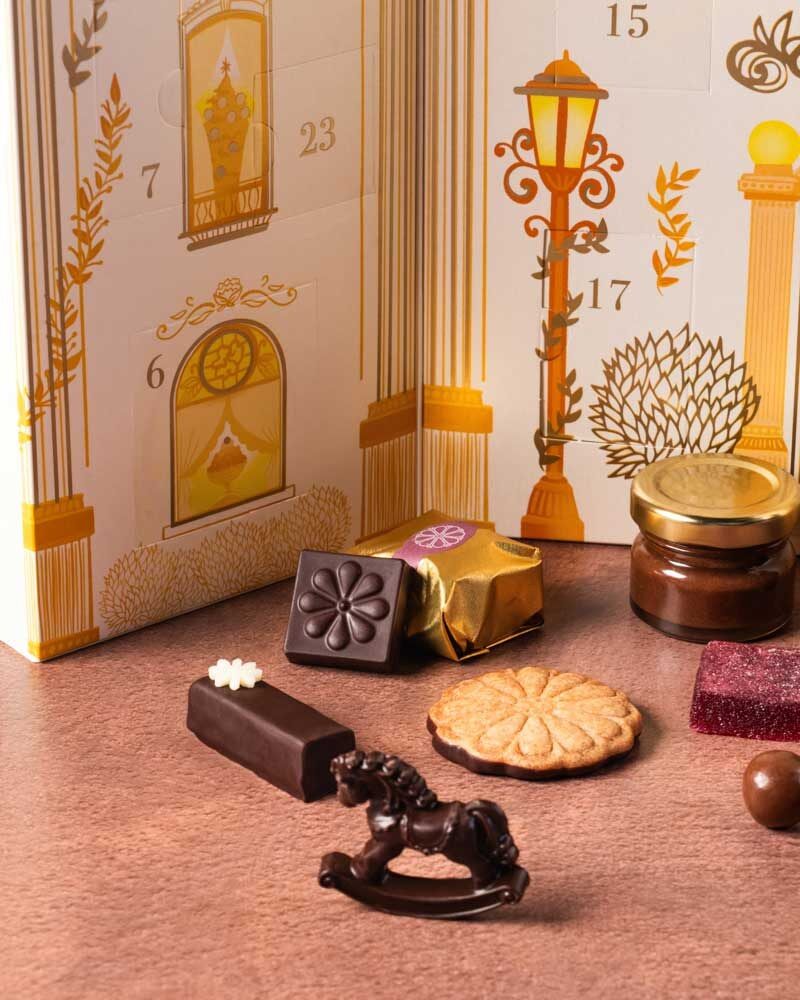 Gros plan sur des chocolats Nina Métayer devant le calendrier blanc et or : Ninourson, mini pot de pâte à tartiner, sablé et pâte de fruits