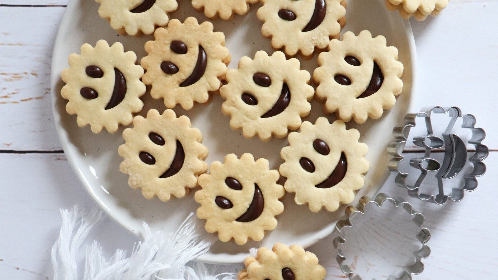 Biscuits sablés en forme de soleils souriants garnis de chocolat dans une assiette, à côté de leurs emporte-pièces