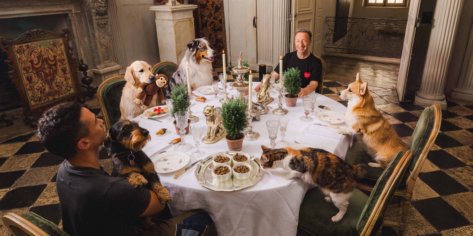 Stéphane Bern et Yori Bailleres à une grande table de château entourés de chiens et d’un chat