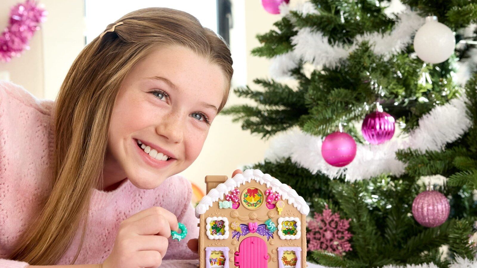 Une fillette sourit devant le sapin de Noël à côté de la maison en pain d’épices du calendrier de l’Avent Polly Pocket