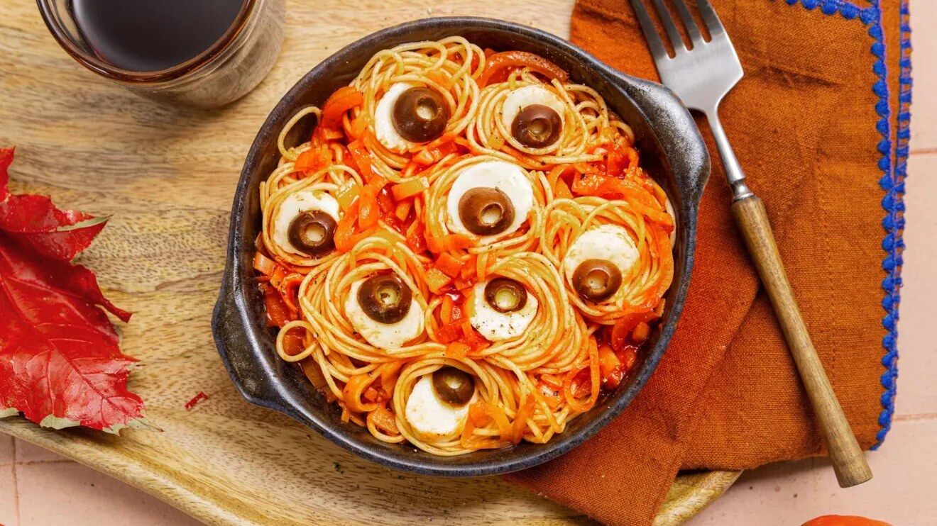 Nids de spaghettis à la sauce tomate avec des yeux en mozzarella et olive dans une cocotte noire, entourés de petites citrouilles