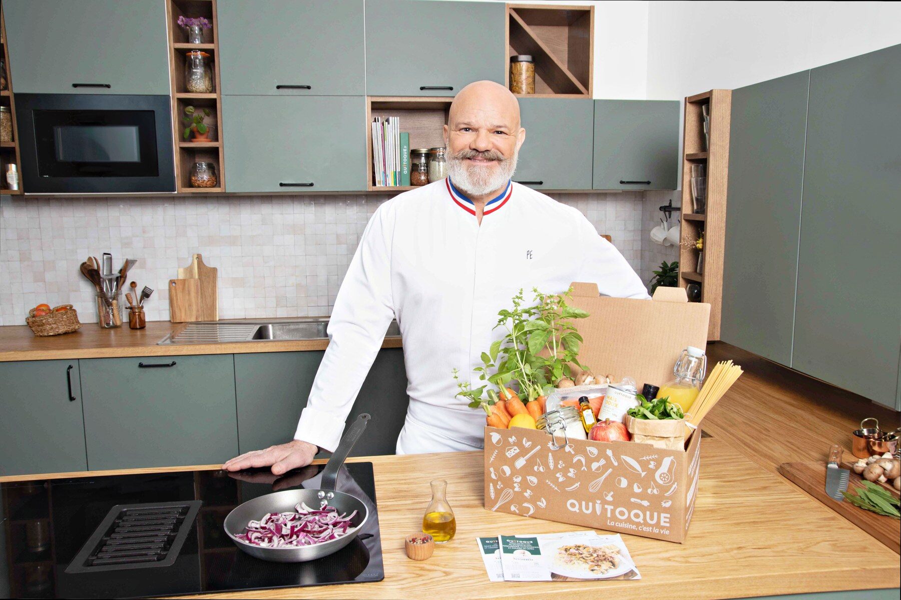 Le Chef Philippe Etchebest dans une cuisine, derrière une box Quitoque ouverte et ses ingrédients frais