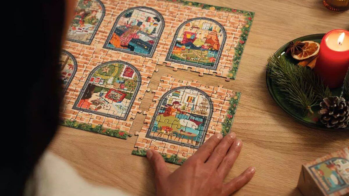 Puzzles de Noël du calendrier de l’Avent Ravensburger 2026 assemblés sur une table près d’une bougie