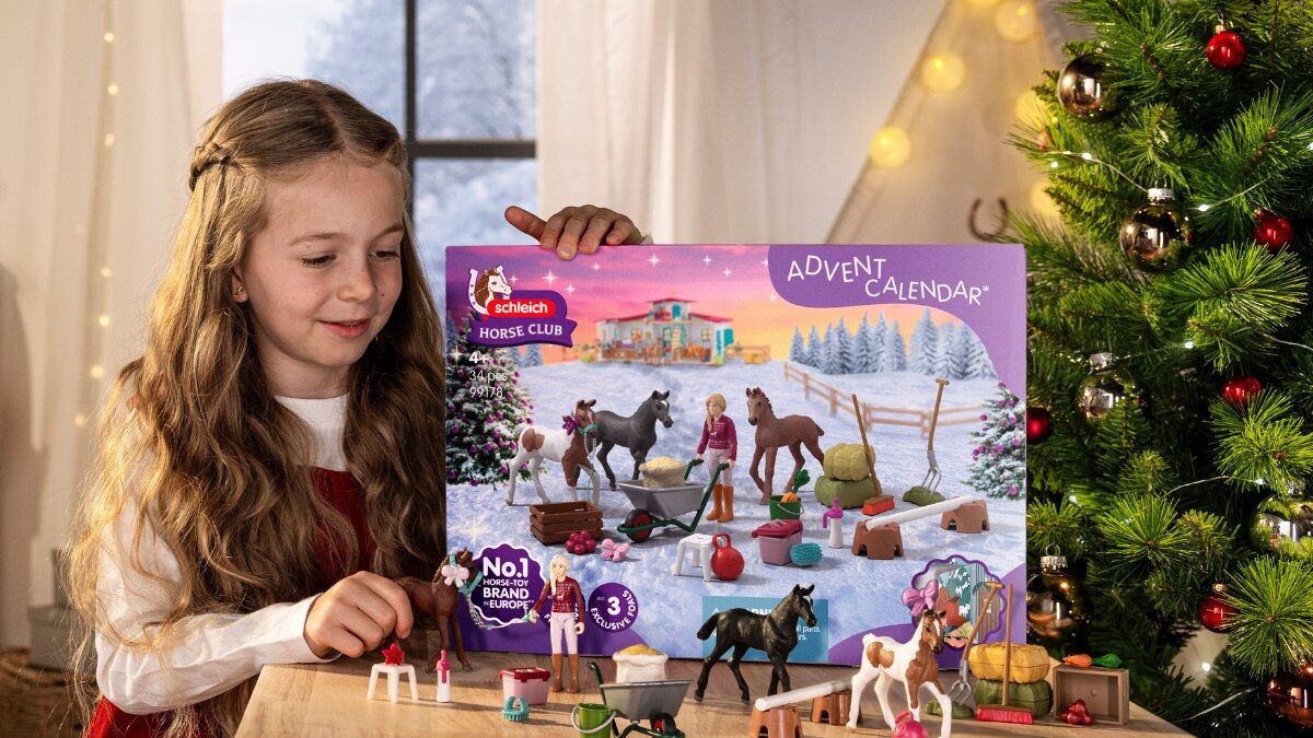Une petite fille joue avec les poulains du calendrier de l’Avent Schleich Horse Club posé sur une table, devant un sapin de Noël illuminé